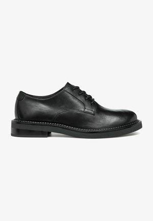 Chaussures habillées en cuir noir avec un bout arrondi, design à lacets et texture lisse. Dotées d'un petit talon et d'un détail de couture contrastant.