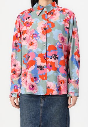 Skjorte med knapper og lange ærmer med stort blomstermønster i rød, pink, blå og lilla på en dæmpet grøn baggrund, båret med denimnederdel.