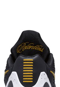 Zwarte sneaker met een gestructureerd bovenwerk, gouden accenten, stekelige gele strepen bij de hiel en het woord "Relentless" in gouden stiksel.