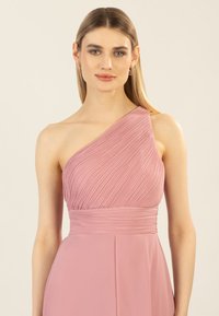 Ein ärmelloses Kleid in zartem Rosa, mit plissierter Textur und einem figurbetonten Taillenbund. Glattes Material mit einem fließenden Rock.
