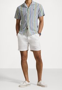 Košile s krátkým rukávem se zapínáním na knoflíky a mnohobarevnými svislými pruhy, spárovaná s bílými lněnými šortkami a bílými teniskami.