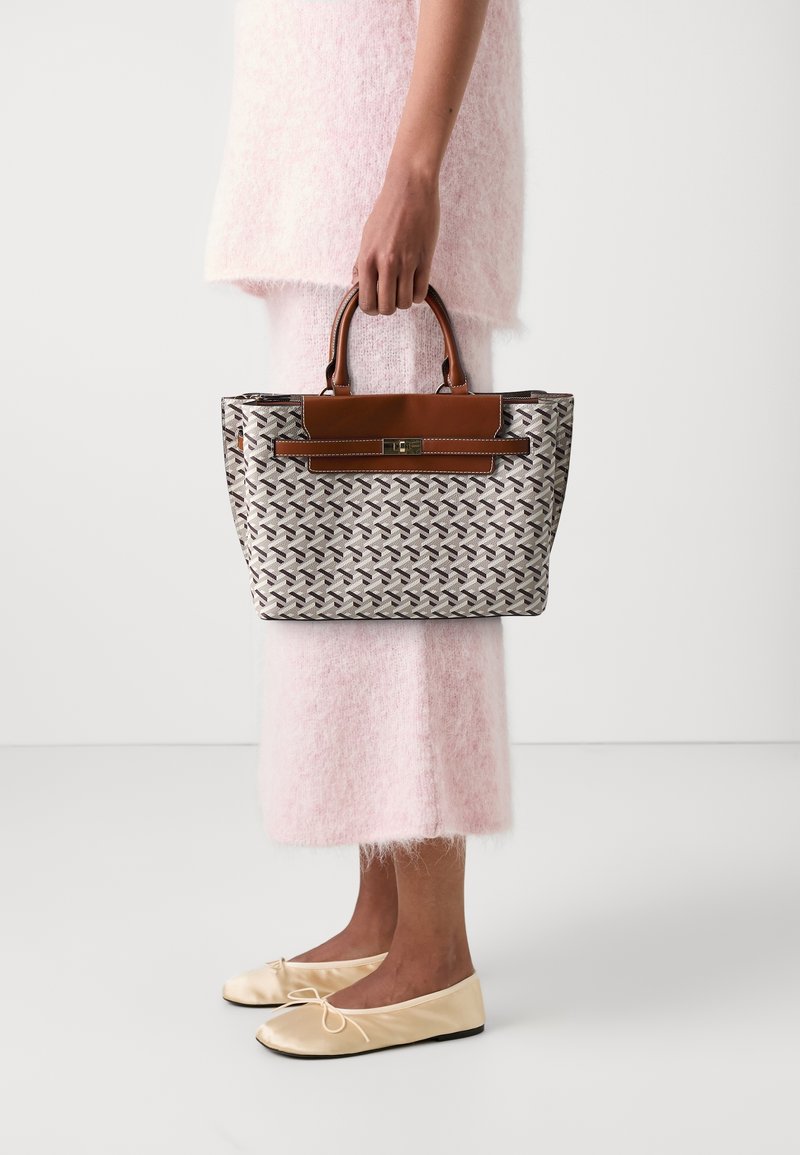 Personne portant une robe rose duveteuse et des ballerines beiges tenant un sac à main à motifs avec des poignées et finitions en cuir marron.
