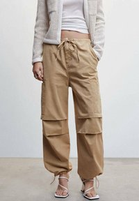 Pantalons cargo beiges avec taille à cordon, deux grandes poches latérales et poignets élastiques. Fabriqués en tissu durable, présentant une coupe décontractée.