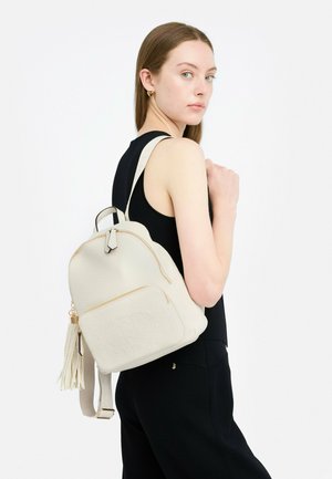 Zaino in pelle beige con superficie testurizzata, chiusure a zip, una tasca frontale e un accento a frange. Spallacci regolabili e forma arrotondata.