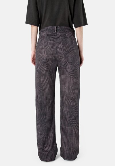 Person, die hoch taillierte, weit geschnittene Hosen mit einem dunklen Karomuster und ein schwarzes Dreiviertelarm-Oberteil trägt, von hinten gezeigt.