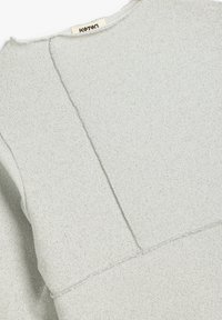 Jasnoszary sweter wykonany z teksturowanej tkaniny. Posiada okrągły dekolt, widoczne szwy oraz lekko luźny krój z naszywanymi detalami.