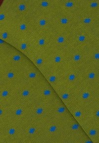 Grüner Stoff mit kleinen blauen Punkten und einer feinen Textur. Das Design zeigt ein sich wiederholendes Muster von gleichmäßig verteilten Punkten.