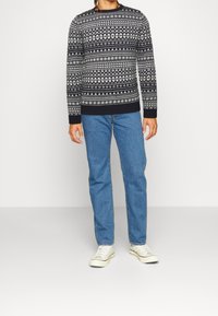 Pull en laine noir et blanc avec des motifs géométriques, col rond et poignets côtes, associé à un jean bleu et des baskets blanches.
