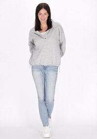 Lysegrå, hættejakke med lynlås, afslappet pasform og lange ærmer, parret med tætsiddende lyseblå jeans og hvide sneakers.