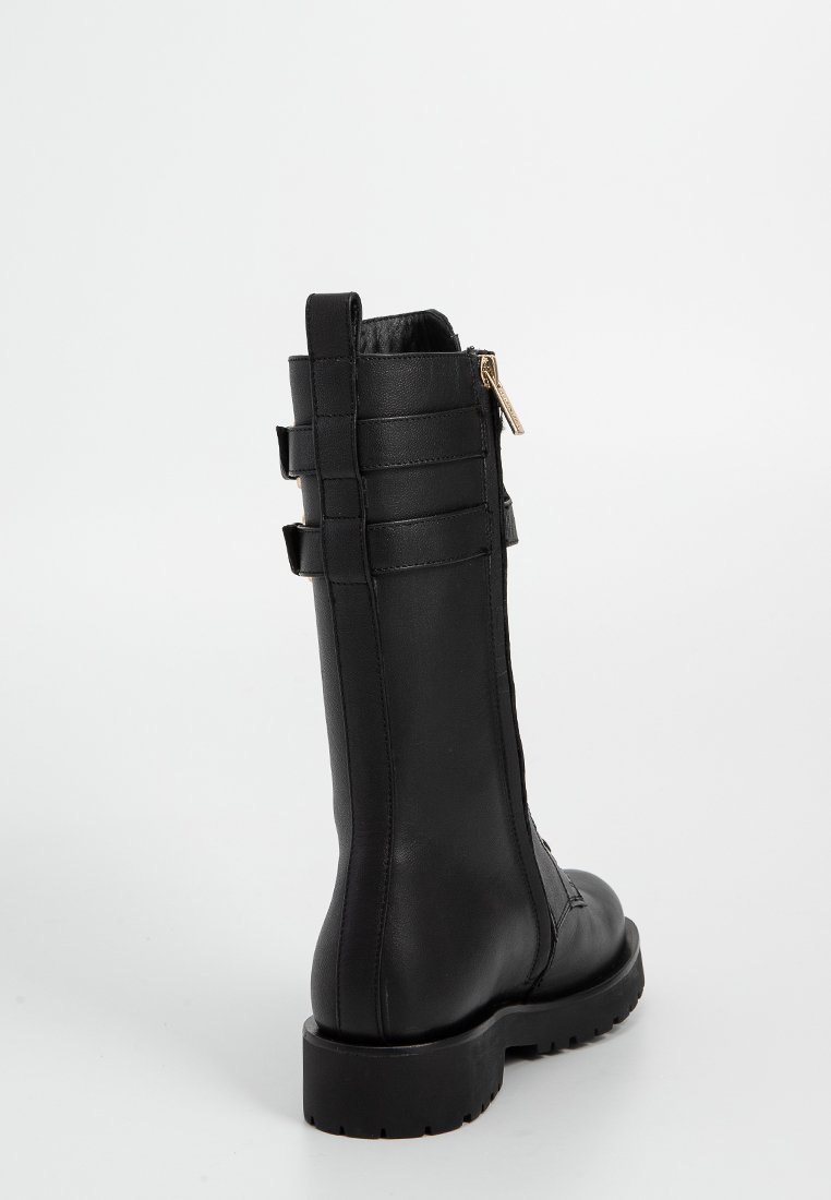 Botte en cuir noir avec une semelle épaisse, une fermeture éclair et des détails de sangle horizontale le long de la tige. Texture lisse avec une finition mate.