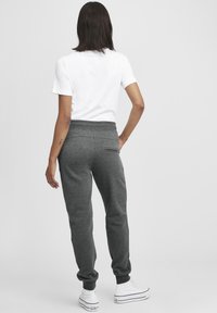 Grå sweatpants med elastisk midjeband och avslutade anklar. Har en bakficka, ihopparad med en enkel vit t-shirt och vita sneakers.