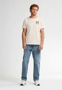 Krémové tričko s vícebarevným motivem na levé straně hrudi, doplněné světle modrými džínami a bílými teniskami. Jednoduchý, ležérní design.