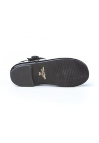 Suela de zapato de cuero negro con una superficie texturizada y surcos. Texto en relieve que dice "Hecho en España" y talla "22" en dorado.