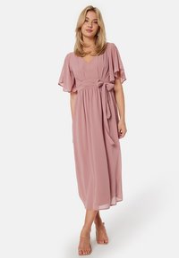 Robe maxi en chiffon rose doux, dotée de manches flottantes, d'une ceinture nouée à la taille et d'une silhouette évasée fluide. Texture lisse et légère.