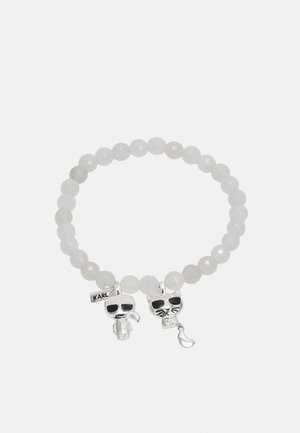 Armbånd lavet af runde hvide perler med to sølvcharms, der bærer sorte solbriller, den ene formet som en person, den anden som en kat.