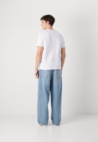 Camiseta blanca de manga corta con cuello redondo, combinada con vaqueros de pierna ancha de color azul claro. Tejido suave con un corte relajado. Diseño básico sin adornos.