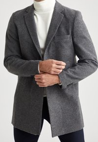 Grå uldblanding blazer med notch lapels, enkelt brystlomme og knaplukning ved ærmerne, parret med en hvid rullekrave sweater under.