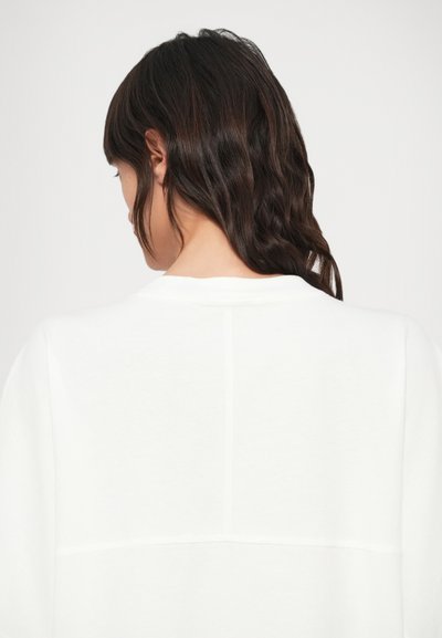 Λευκό φούτερ με άνετη εφαρμογή, στρογγυλή λαιμόκοψη, λεία υφή και λεπτομέρειες ραφής στο πίσω μέρος.