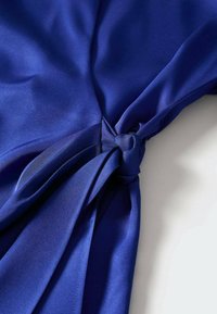 Tissu bleu royal au toucher lisse, présentant un détail de nœud sur un côté. Le design comprend des plis s'étendant à partir du nœud.