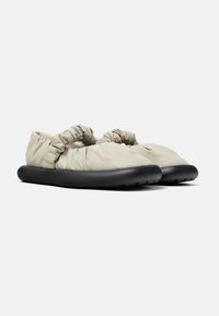 Scarpe slip-on beige chiaro con tomaia arricciata e suola nera imbottita. Presentano una texture liscia e due cinture decorative.