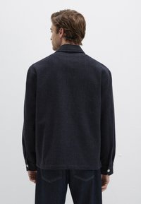 Marineblaue gewebte Jacke mit strukturiertem Muster, langen Ärmeln und Reverskragen. Verfügt über Druckknöpfe an den Manschetten und ein lockeres Schnittdesign.