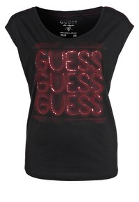 Sort kortærmet t-shirt med skinnende røde palietter, der stavrer "GUESS" flere gange. Blødt stof, rund halsudskæring og afslappet pasform.