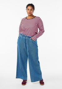 Chemise à rayures à manches longues en rose et marron, associée à un jean large bleu. Le jean est doté d'une taille élastique et de poches.
