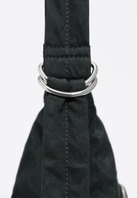 Czarny materiałowy pasek plecaka z metalowymi srebrnymi pierścieniami. Charakteryzuje się widocznym szyciem i fakturą, podkreślając trwały design.