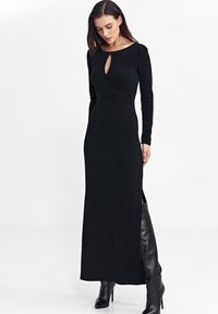 Czarna sukienka z długim rękawem, z dekoltem w kształcie łezki, dopasowany krój, teksturowana tkanina i boczne rozcięcia, w połączeniu z czarnymi, wysokimi na kolano botkami.