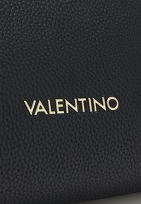 Czarna torba ze skóry o strukturze tekstury, z nazwiskiem "VALENTINO" w złotych literach. Powierzchnia prezentuje wzór w małe kamyki.