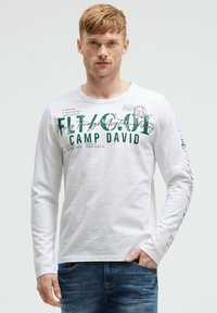 White long-sleeve T-shirt with green graphic text and print. Soft fabric with a crew neck, featuring detailed text on sleeves and front.