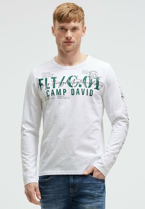 Weißes Langarm-T-Shirt mit grünem Grafiktext und Druck. Weicher Stoff mit Rundhalsausschnitt, ausgestattet mit detailliertem Text an den Ärmeln und auf der Vorderseite.