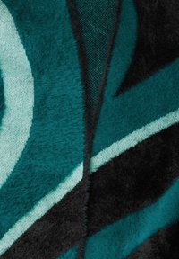 En texturerad filt med djärva, abstrakta mönster i teal, svart och ljusgrön, som visar en blandning av mjuka och släta ytor.