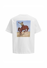 Camiseta de algodón blanca con un gráfico colorido de un vaquero montando un caballo rojo contra un cielo azul, con un sutil fondo arenoso.