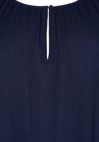 Marinblus med veckad textur, nyckelhålöppning bak och en svart knappstängning vid halsen. Lättviktsmaterial.