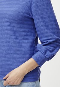 Kuningas sinine pullover reljeefsete triipudega, ümar dekoltee ja kergelt kogutud, mansettidega varrukad. Kangas näeb välja pehme ja hingav.