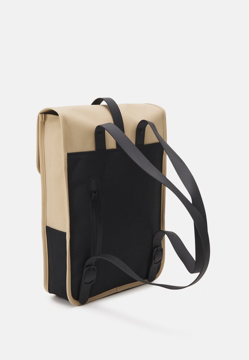 Sac à dos avec un extérieur synthétique beige, des côtés en tissu noir, des bretelles noires réglables et une fermeture à rabat. Présente un design et des textures minimalistes.