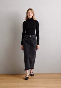 Top a collo collo nero abbinato a una gonna di denim nera a vita alta. La gonna presenta una linea dritta e un orlo sfilacciato. Scarpe basse nere.