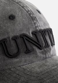 Grijze stoffen pet met zwarte geborduurde tekst "UNITED." De textuur is zacht, met zichtbare stiksels en een gebogen klep.