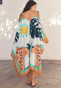 Luźny, lekki kaftan w pastelowych kolorach z motywami lamparta i słońca, z wiązaniami na ramionach i kontrastowym wykończeniem.