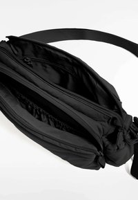 Zwarte nylon tas met meerdere ritscompartimenten, elastische details en een verstelbare strap. Gladde textuur, compact ontwerp.