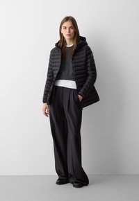 Giubbotto puffa nero con cappuccio, caratterizzato da un design a righe orizzontali. Abbinato a un maglione a maglia grigio scuro e pantaloni neri a gamba larga su misura.