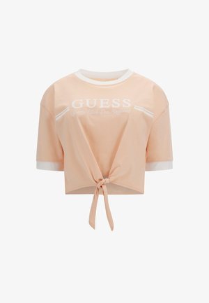 Crop top pêche en tissu doux, avec un col rond blanc et un ourlet blanc, imprimé du logo "GUESS" et un détail noué à l'avant.
