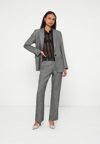 Szary garnitur w kratę z dopasowaną marynarką i prostymi spodniami, nałożony na prześwitujący czarny top. Uzupełniony wąskim czarnym paskiem i jasnymi szpilkami.