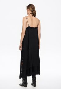 Musthave muströöpidega must sleeveless kleit, voolav disain, kihiline kangas ja külgsisepistmed. Mudel kannab pikki musti saapaid.