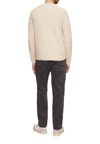 Lichtbeige langluipaard top met een ronde halslijn, gecombineerd met donkergrijze broeken. De outfit is afgemaakt met wit en beige sneakers.