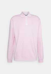 Světle růžová polokošile s dlouhým rukávem, zapínáním na knoflíky a jemně vyšitým logem na levé straně hrudi na bílém pozadí.