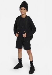 Svart sportoutfit som inkluderar en långärmad tröja, shorts och sneakers. Tillbehör: en svart mössa och en svart ryggsäck.