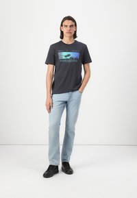 Svart bomull T-skjorte med et fargerikt grafisk trykk av palmer. Kombinert med lyseblå denimjeans og svarte joggesko. Enkelt design.