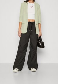 Světlý zelený blejzr, bílý crop top a černé kalhoty s širokými nohavicí. Černá kabelka s flitry. Masivní bílé tenisky. Jednoduchý design bez vzorů.